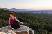 Молодая женщина йога практикует йогу на скале в горах со светом восхода солнца — стоковое фото