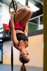 Jeune athlète féminine en tenue de sport travaillant les yeux fermés sur un appareil de gymnastique avec anneaux dans un gymnase — Photo de stock