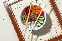 From above white bowl with tasty poke dish and chopsticks placed behind frame on table covered with sesame seeds — Stock Photo