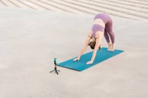 Unrecognizable flexible female practicing yoga in Adho mukha svanasana and stretching body during online yoga class — Stock Photo