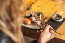 From above cropped unrecognizable female eating tasty sushi in Japanese restaurant while sitting at wooden table — Stock Photo