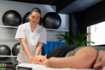 Щасливий масажист в білому халаті масажуючи теля жіночого пацієнта врожаю під час сеансу фізіотерапії в клініці — стокове фото