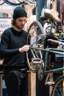 Vue latérale de la roue de réparation masculine grave du vélo tout en travaillant en atelier — Photo de stock