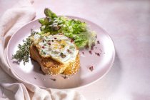 Високий кут смаженого яйця на бріосі, який подається на тарілці зі свіжим салатом для апетитного сніданку на рожевому фоні — стокове фото
