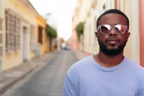 Portrait of stylish African American man walking with sunglasses outdoors. Fashionable black man in the street. — Stock Photo