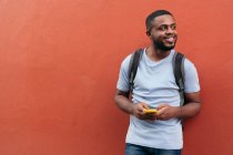 African Man with backpack and mobile phone smiling while leaning on wall — Stock Photo