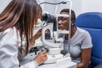 Augenoptiker beim Einstellen des Retinographen während der Untersuchung des Sehvermögens einer schwarzen Frau — Stockfoto