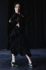 Mujer joven y elegante en traje negro bailando flamenco mientras mira a la cámara - foto de stock