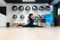 Full body side view of focused young female in activewear doing Front Splits pose and keeping hands in namaste position while practicing mindfulness during yoga class in studio — Stock Photo