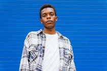 From below serious dreamy African American male standing looking at camera on background of blue wall in street — Stock Photo