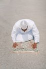 Unerkennbarer muslimischer Mann kniet auf Teppich und berührt Boden mit der Stirn, während er an sonnigen Tagen am Sandstrand betet — Stockfoto