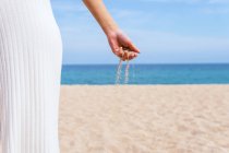 Cortar hembra anónima con un puñado de arena corriendo a través de los dedos de pie en la orilla del mar en verano - foto de stock