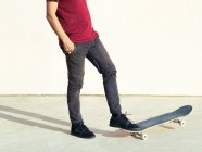 Cropped unrecognizable male skateboarder with hands in pockets looking away on pavement in sunlight on beige background — Stock Photo