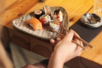 De cima cortado fêmea irreconhecível comer sushi saboroso no restaurante japonês, enquanto sentado à mesa de madeira — Fotografia de Stock
