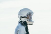 Vista lateral del hombre en traje espacial y casco mirando hacia otro lado mientras está parado en el camino en el día soleado en la naturaleza - foto de stock
