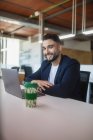 Веселый мужчина-предприниматель смотрит в камеру, работая на рабочем месте, сидя за столом с ноутбуком — стоковое фото