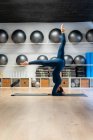 Ganzkörper-Seitenansicht einer fitten Frau in Sportbekleidung, die unterstützte Kopfstand-Variation beim Yoga im Fitnessstudio praktiziert — Stockfoto