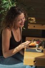 Vista lateral da fêmea sorridente comendo sushi saboroso no restaurante japonês enquanto se senta na mesa de madeira — Fotografia de Stock