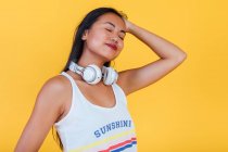 Entzückte Asiatin steht mit geschlossenen Augen auf gelbem Hintergrund im Studio — Stockfoto