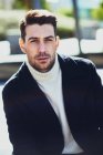 Adult bearded male in sweater and coat on the street looking at camera in city in daytime — Stock Photo