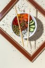 Сверху белая миска с вкусным блюдом и палочками для еды, помещенными за рамкой на стол, покрытый семенами кунжута — стоковое фото