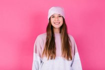 Adolescente mujer feliz con cabello castaño y pañuelo para la cabeza que representa la conciencia del cáncer mirando a la cámara en el fondo rosa - foto de stock