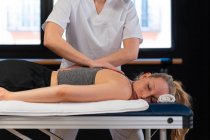 Обрізані невпізнавані масажистки посміхаються і масажують плечі жінки під час роботи в клініці фізіотерапії — стокове фото