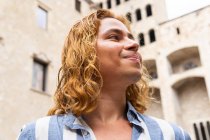 From below peaceful happy male with long hair standing in street and enjoying freedom while looking away — Stock Photo