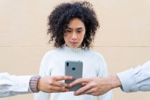 Безликі різноманітні люди тримають смартфон перед молодою етнічною жінкою з кучерявим волоссям — стокове фото