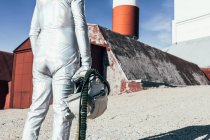Back view an in spacesuit standing on rocky ground against striped rocket shaped antennas on sunny day — Stock Photo