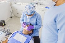 From above of anonymous female doctor in uniform cleaning teeth of male patient with dental retractor in hospital — Stock Photo