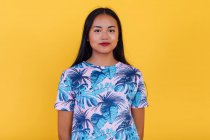 Портрет азіатської жінки, що стоїть на жовтому тлі в студії, дивлячись на камеру — стокове фото
