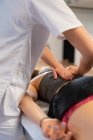 Зверху обрізаний невпізнаваний масажист посміхається і масажує жінку під час роботи в клініці фізіотерапії — стокове фото