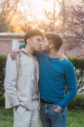Vista lateral de la pareja homosexual encantada de hombres besándose y mirándose en el parque - foto de stock