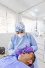 Stomatologue féminine en uniforme et masque respiratoire durcissant les dents du patient masculin à l'hôpital — Photo de stock