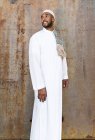 Ісламський чоловік в автентичному білому одязі, стоячи проти брутальної стіни. — стокове фото