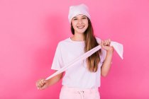 Unbekümmerte weibliche Jugendliche in lässiger Kleidung mit braunen Haaren und Kopftuch stehen für Konzeptbewusstsein und schauen in die Kamera, die auf rosa Hintergrund steht — Stockfoto