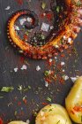 Vue de dessus du tentacule de poulpe frit et des morceaux de pomme de terre servis avec des épices sur un plateau noir sur la table — Photo de stock