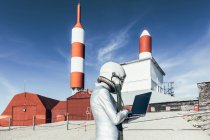 Side view male astronaut in spacesuit browsing data on netbook while standing outside station with rocket shaped antennas — Stock Photo