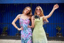 Молодые модные подруги в летних платьях и солнцезащитных очках стоят вместе на городской улице и смотрят в камеру — стоковое фото