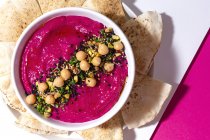 Top view of appetizing beetroot hummus garnished with chickpea served on two colored background with bread — Stock Photo