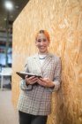 Smiling female entrepreneur standing with computer near wall in coworking space while looking at camera — Stock Photo