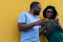 Black couple using a mobile phone leaning against a yellow wall — Stock Photo