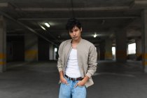 Ritratto di giovane latino in abiti casual guardando con fiducia la macchina fotografica con le mani sulle tasche mentre in piedi nel parcheggio — Foto stock