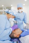 Stomatologin in Uniform und Atemmaske heilt Zähne eines männlichen Patienten im Krankenhaus — Stockfoto