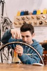 Серьезное мужское механическое закрепляющее колесо говорило, сидя на рабочем месте в обслуживании велосипедов — стоковое фото