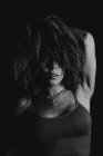 Preto e branco encantador modelo feminino afro-americano com cabelo encaracolado olhando para a câmera no estúdio escuro — Fotografia de Stock