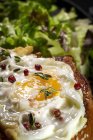 Uovo fritto su brioche servito su vassoio con lattuga fresca per appetitosa colazione su fondo nero — Foto stock