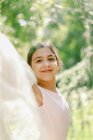 Zufriedene Teenagerin in Ballettkleid und Spitzenschuhen, die an sonnigen Tagen auf einer Wiese im Park mit transparentem Tuch spielt — Stockfoto