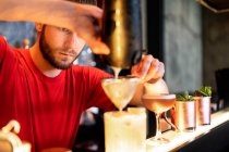 Barman concentré versant cocktail rafraîchissant froid à travers passoire en verre placé sur le comptoir dans le bar — Photo de stock